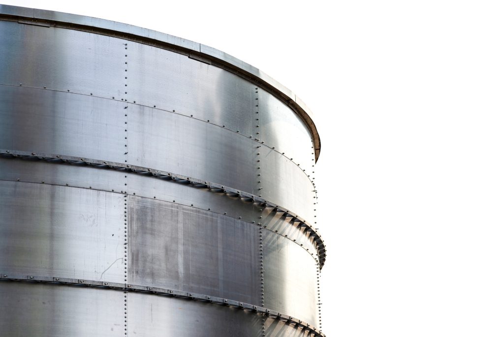 Steel industrial silos for liquids and solids standing in a factory, white sky in the background.